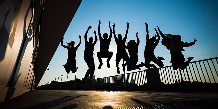 Outline of 7 students jumping excitedly with blue sky in background