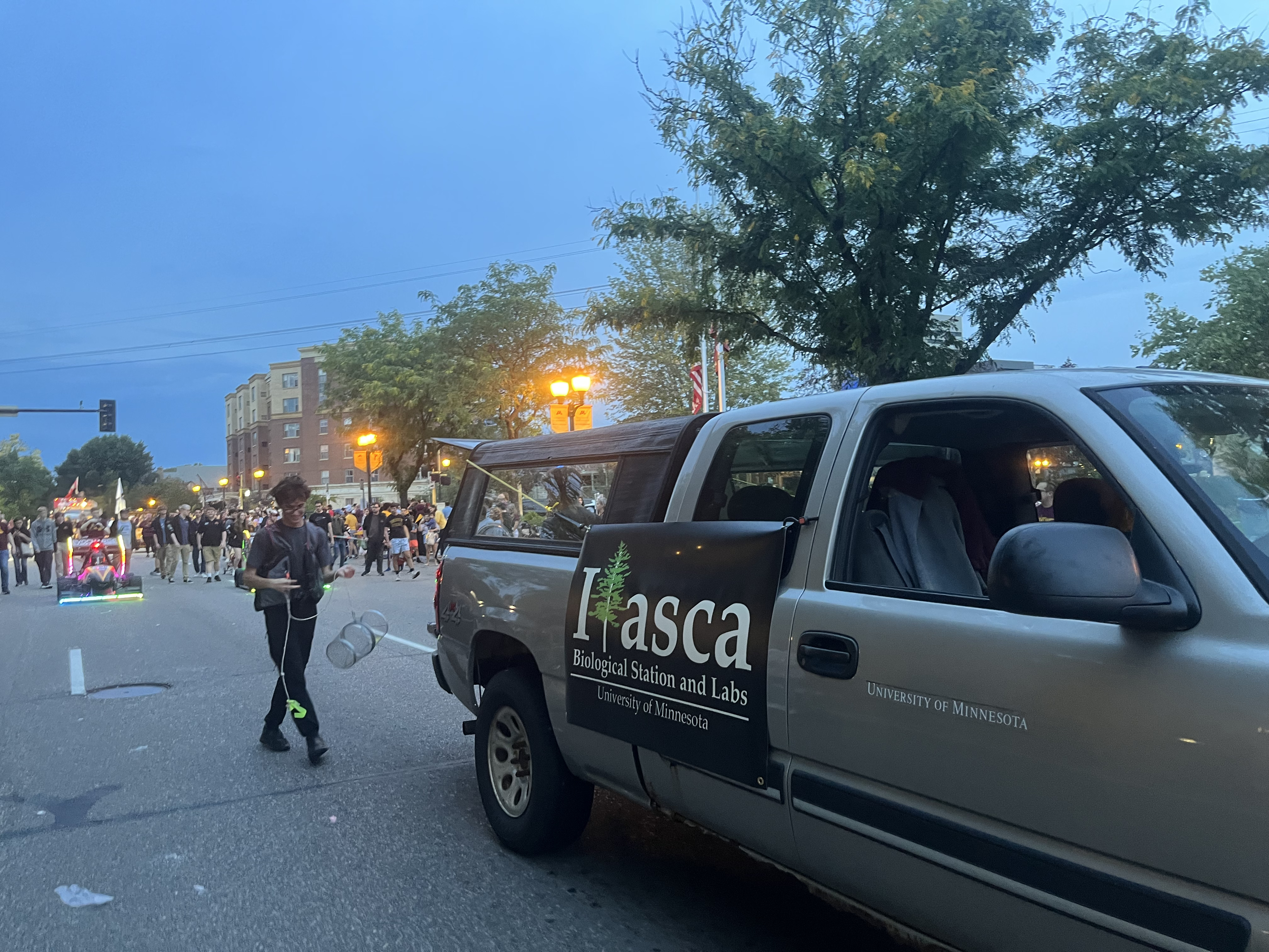 IBSL Booster Club members in the UMN Homecoming Parade. A club member in waders is handing out candy next to a truck with an Itasca banner.