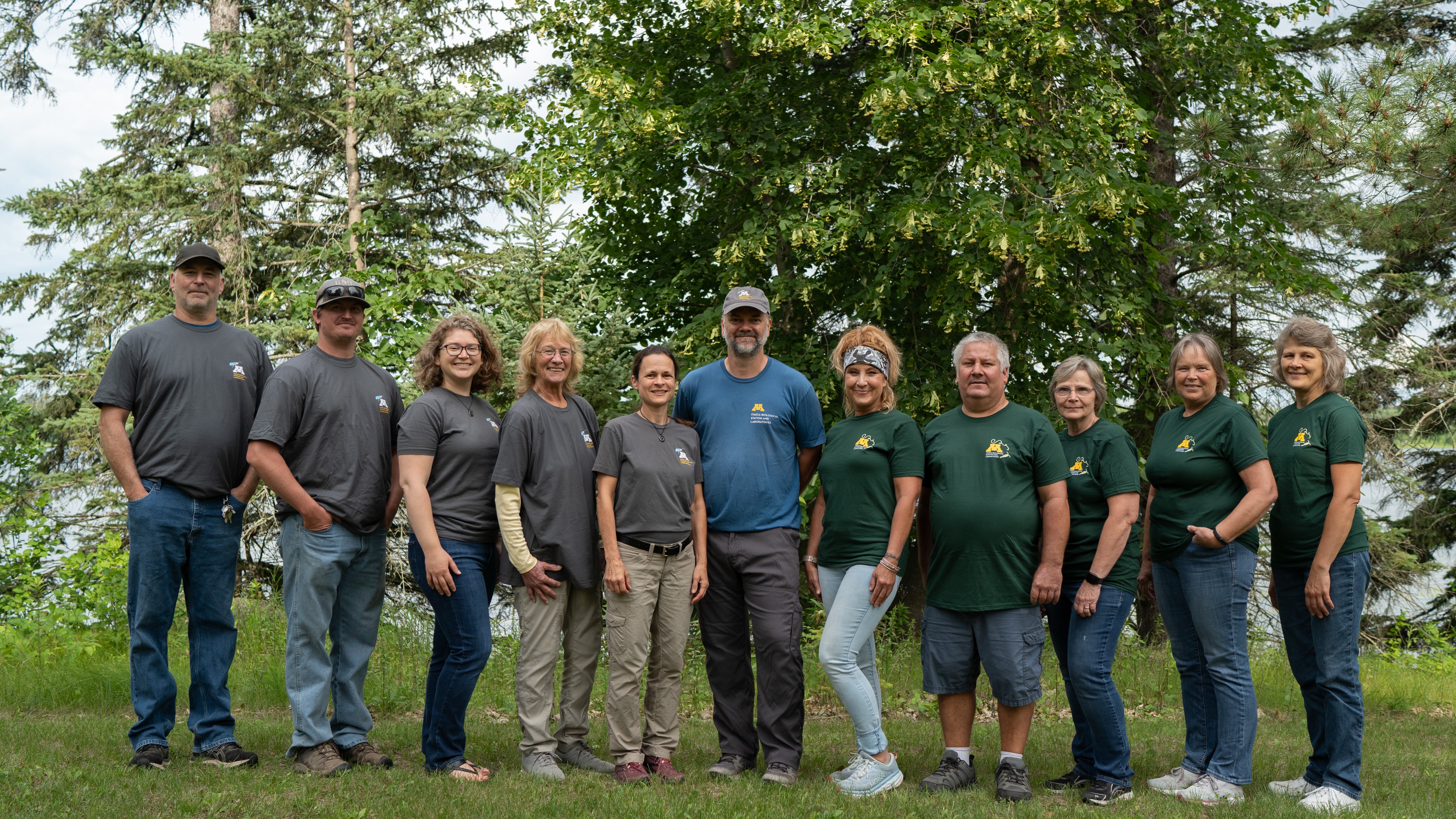 11 people standing in a row with trees behind them