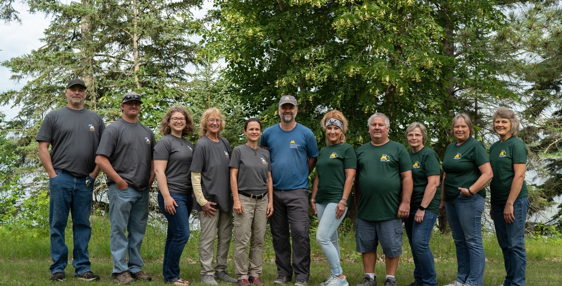 11 people standing in a row with trees behind them