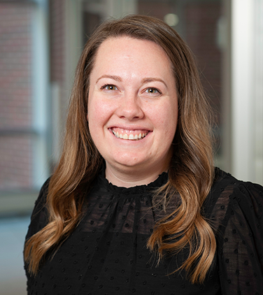 Woman with dark blonde wavy hair smiling wearing a black shirt